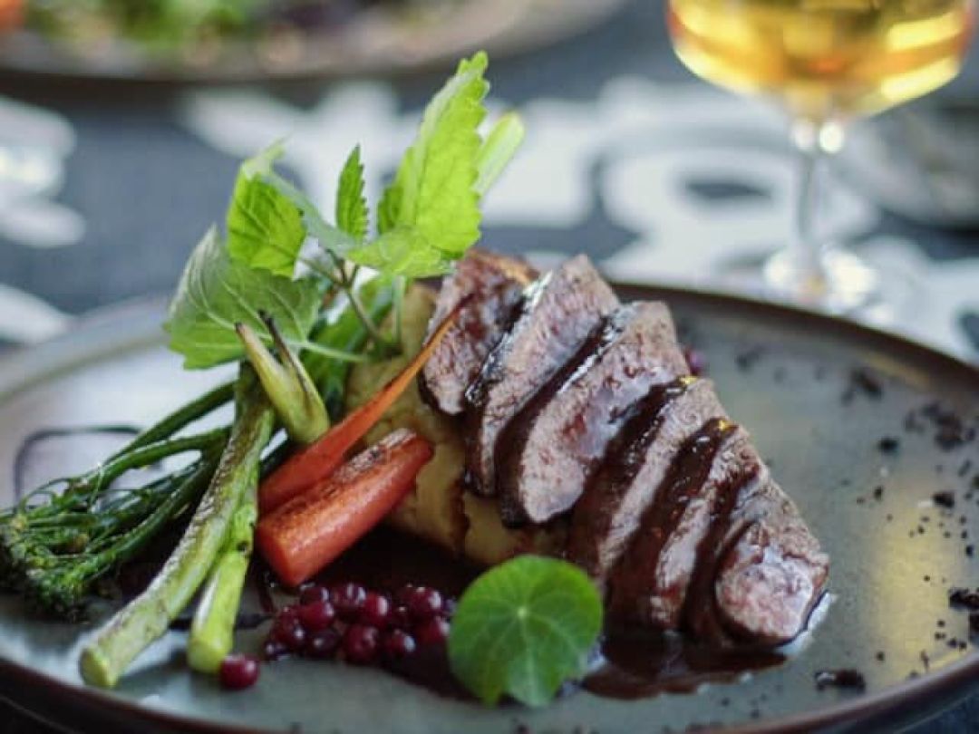 Gourmet dish with sliced meat, vegetables, and garnish on a black plate.