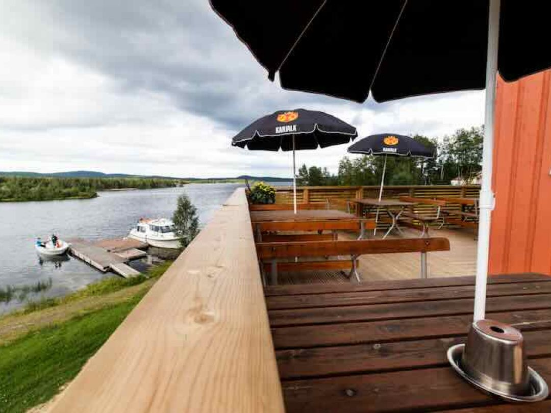 Outdoor terrace with wooden benches and umbrellas overlooking a lake and boats.