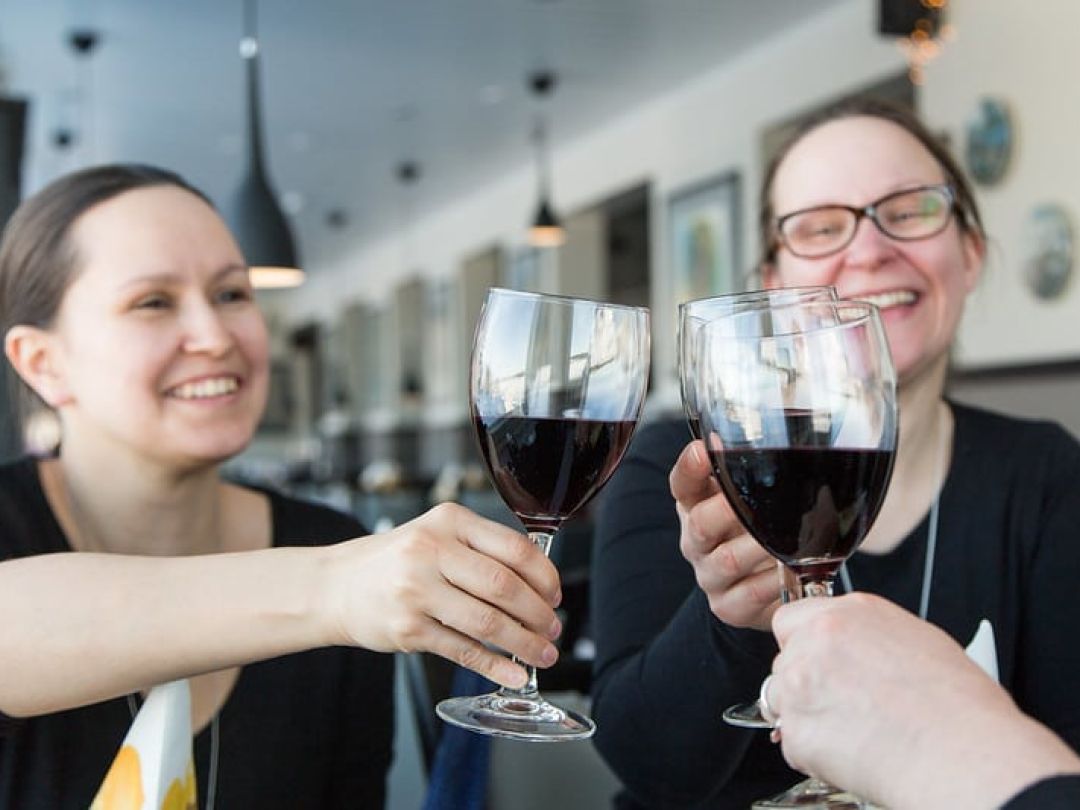 Group of people clinking wine glasses and smiling at a restaurant.