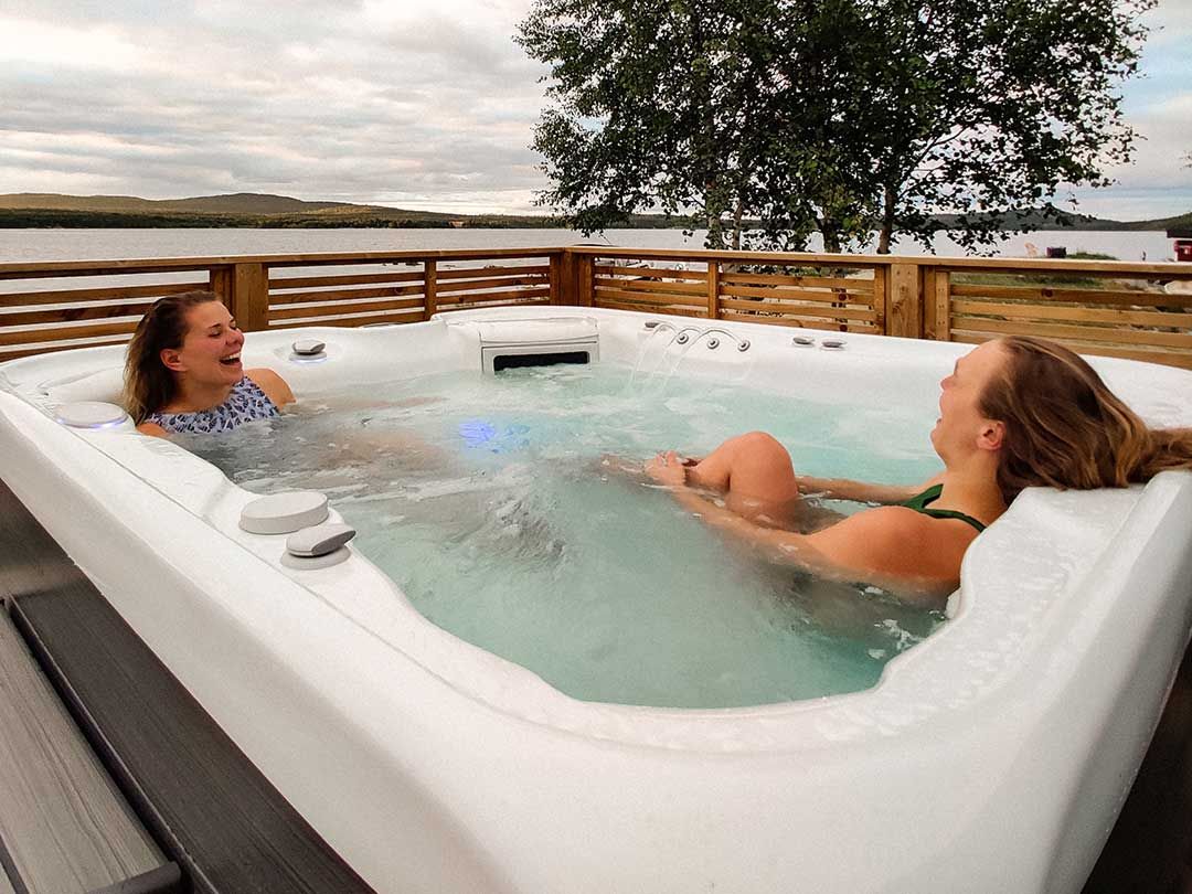 Two women enjoying and laughing in hot tub by the lake.