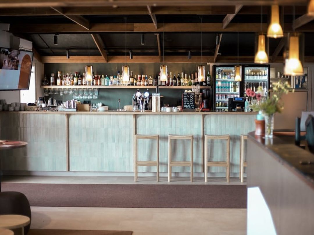 Modern bar interior with bottles on shelves and high chairs.