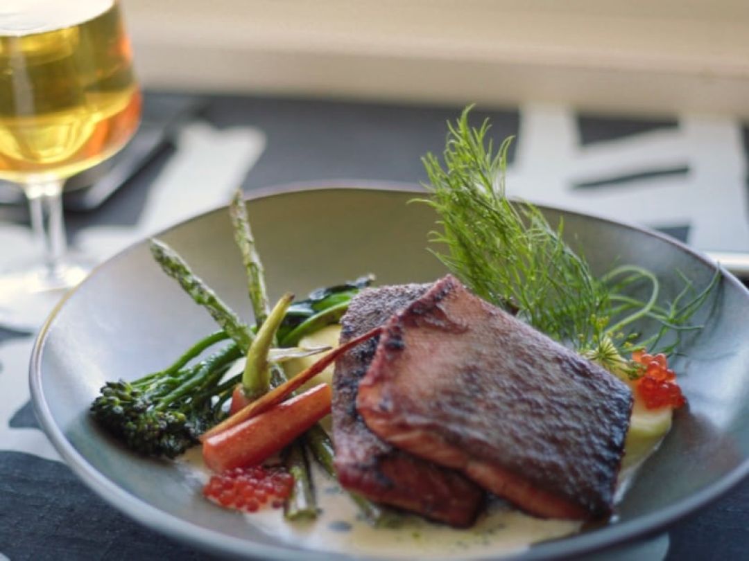 Plate with grilled fish, vegetables, and garnish served with a drink.