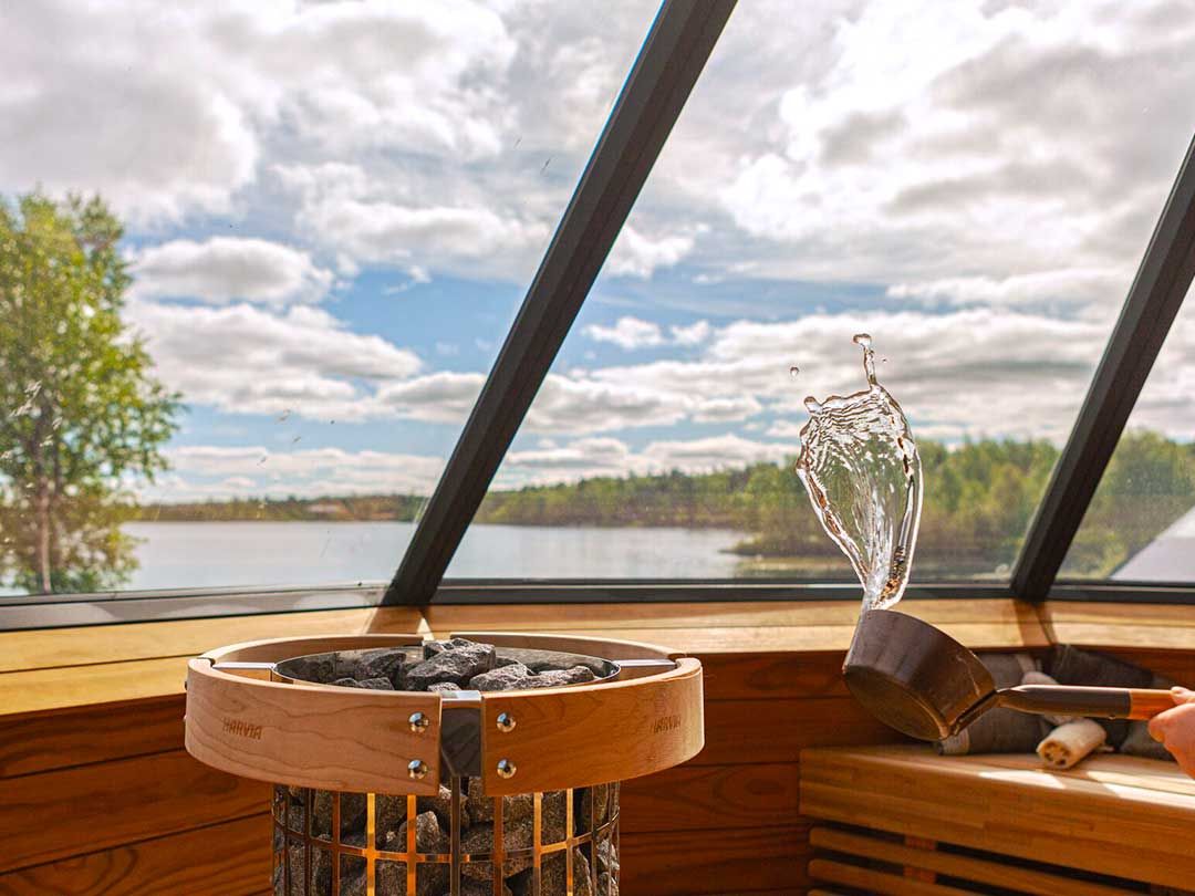 Interior of sauna with a stove and a view through large windows to the lake.