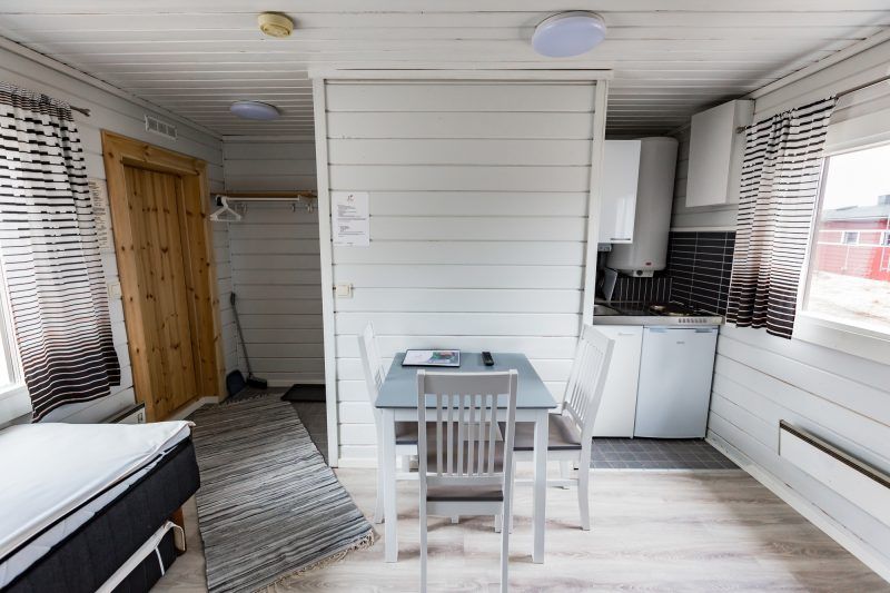 Wooden room with small kitchen, dining table, rug and bed.
